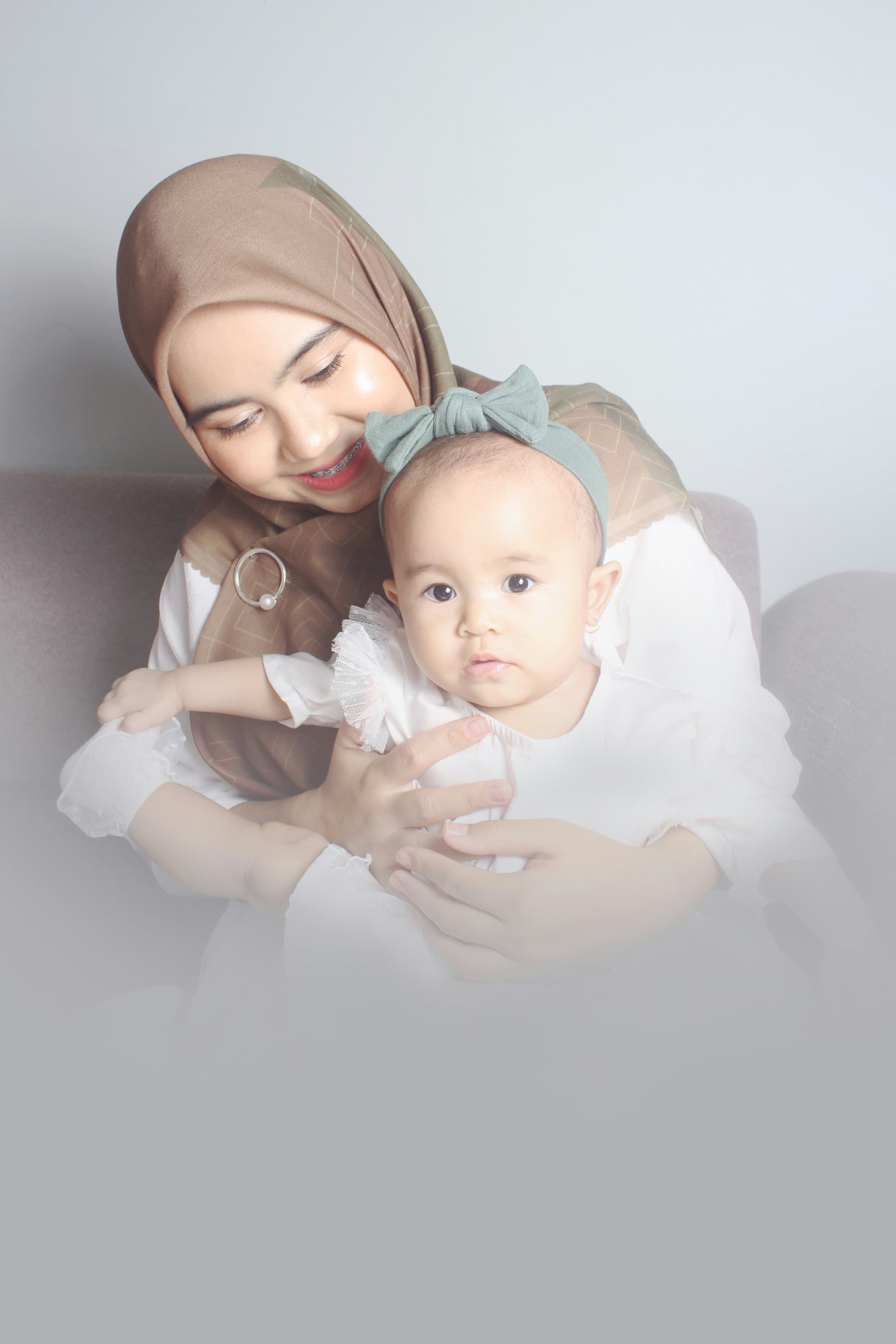 Ibu berhijab tersenyum sambil memangku bayinya